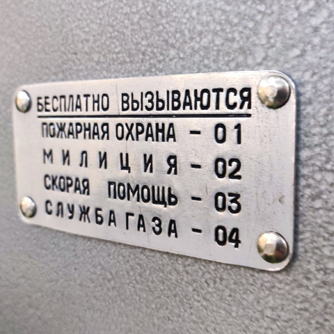 Табличка с номерами экстренных служб на корпусе телефонного автомата