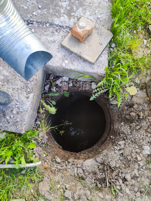 Открытый колодец с водой рядом с выпуском водосточной трубы и разрытым грунтом