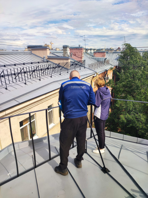 Работы на крыше у ограждения на фоне неба и панорамы городских домов