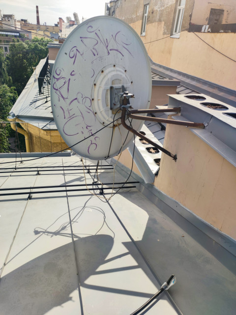 Спутниковая антенна с кабелями на металлической крыше у парапета