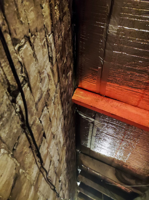 Кирпичная стенка и фольгированная изоляция под кровлей на чердаке, вертикальный кадр