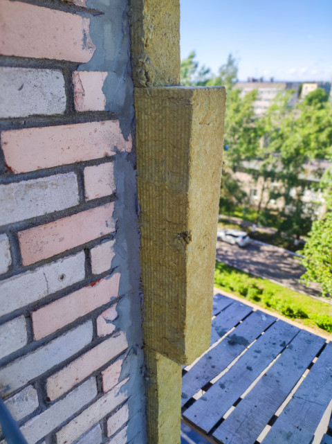 Утепление фасада минеральной ватой на углу кирпичной стены рядом со строительными лесами