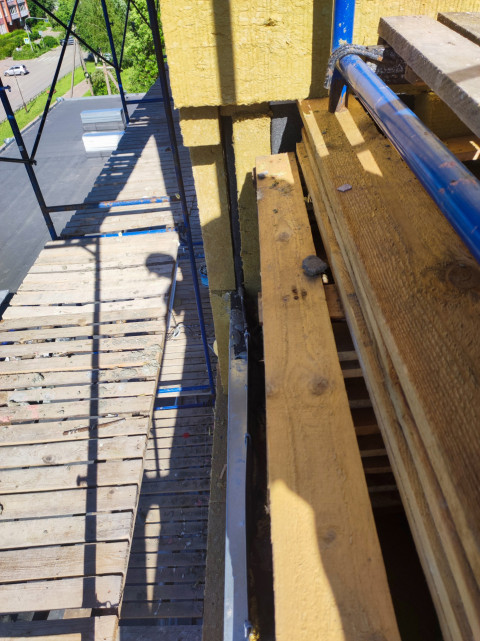 Деревянный настил строительных лесов и штабель досок у утепляемой стены