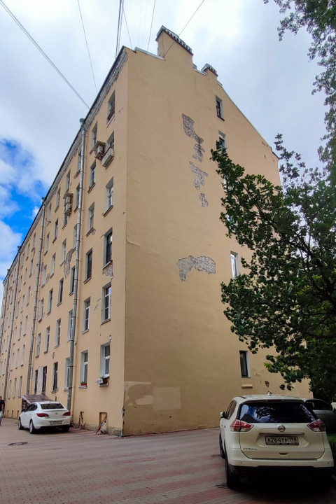 Многоэтажный жилой дом с оголёнными участками штукатурки на торце и припаркованными автомобилями во дворе