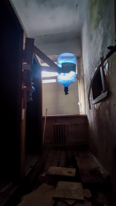 Узкий проход с перевёрнутой бутылью для воды, радиатором и повреждённым полом