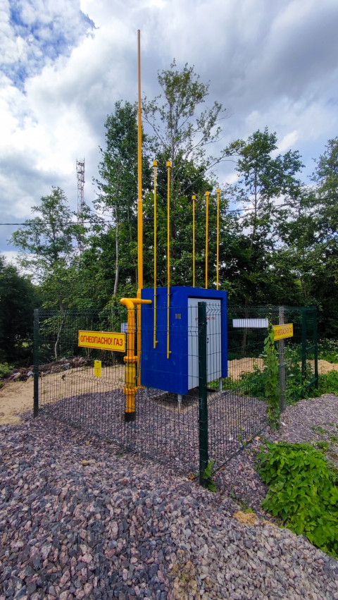 Газовая площадка за ограждением среди деревьев с трубами и шкафом