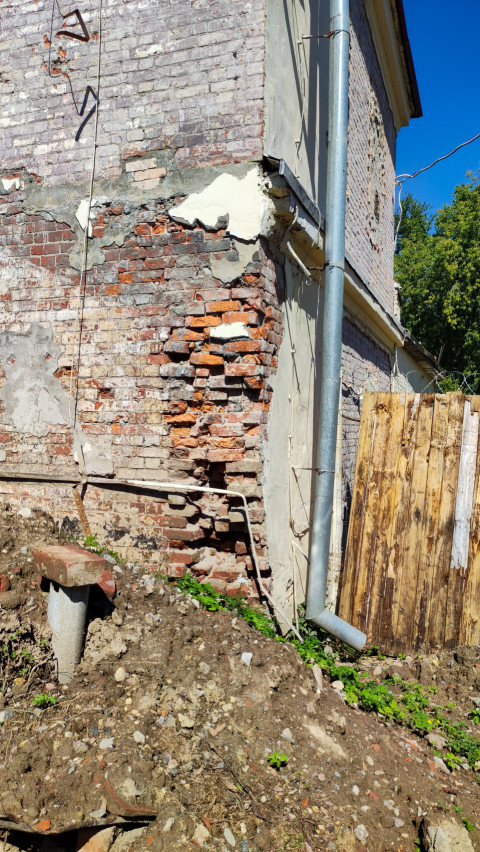 Поврежденная кирпичная стена дома с водосточной трубой