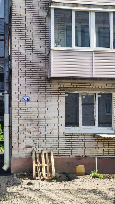 Кирпичный фасад многоэтажки с балконом, окнами и адресной табличкой «207»