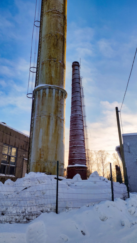 Две промышленные трубы на территории завода зимой