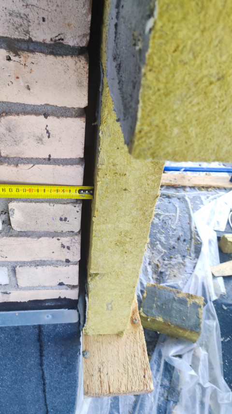 Плита минеральной ваты на подкладке и замер рулеткой технологического зазора у стены
